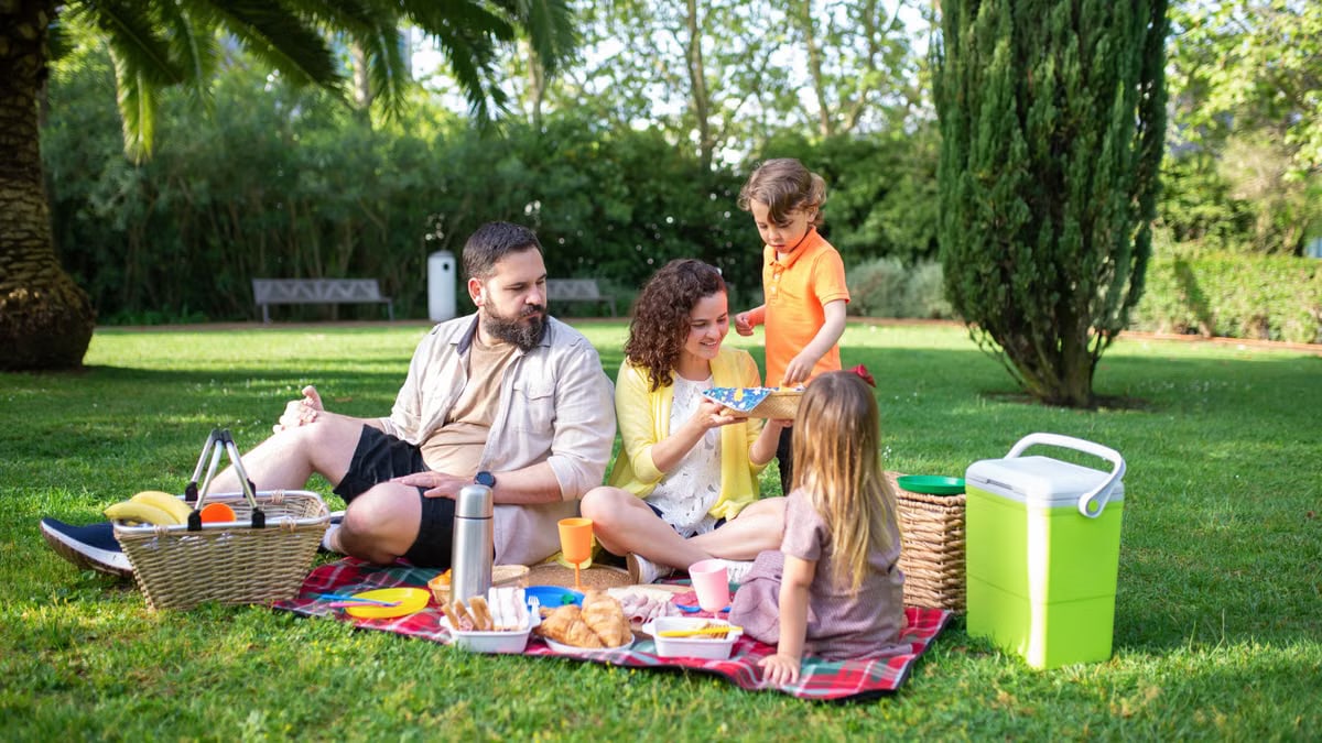 A family having a joyful picnic in a sunny park with fresh food and drinks.